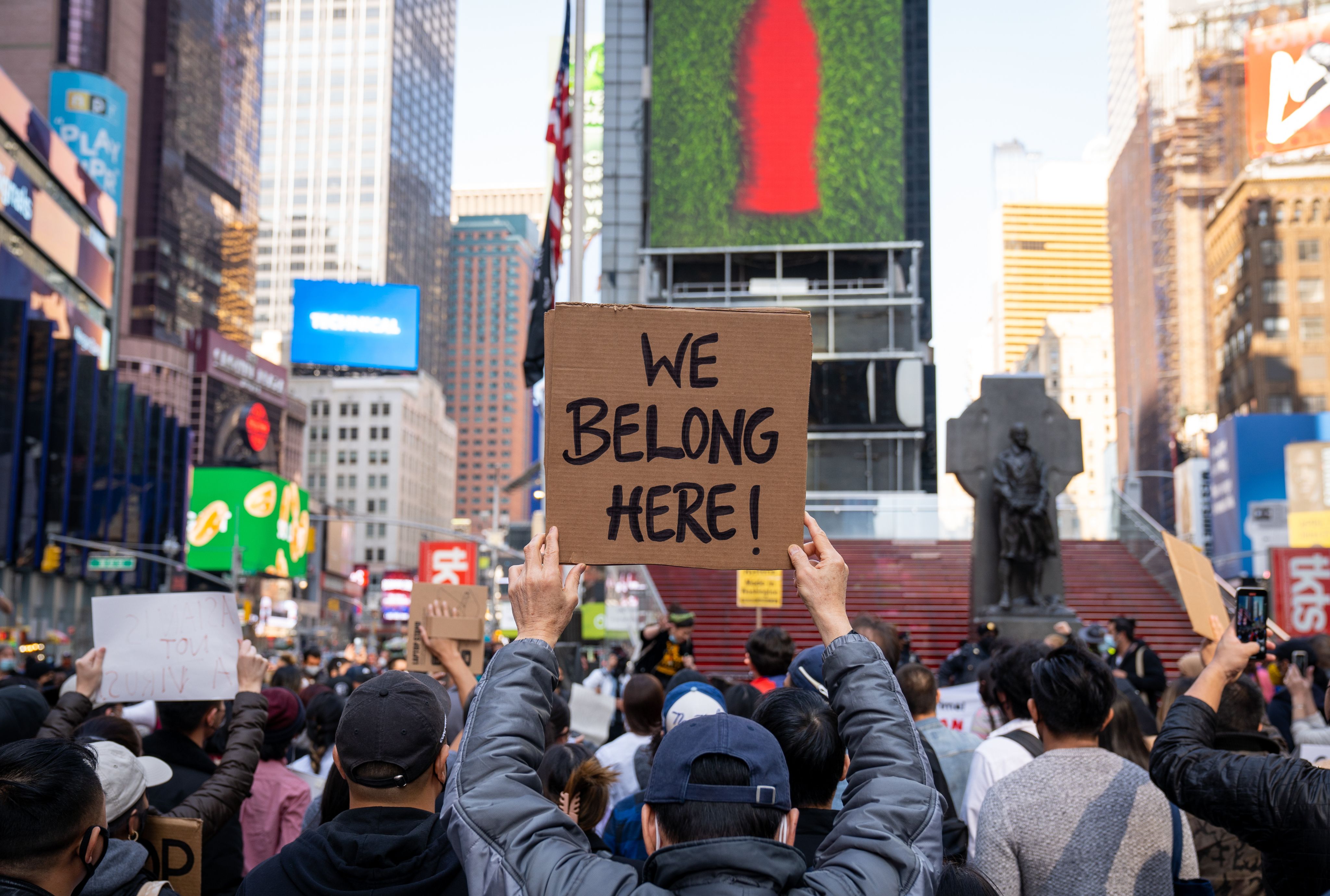 An activist in Times Square holds a sign reading 'We belong here'